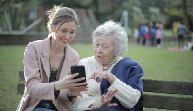 O tânără și o bătrână care se uită la un telefon de pe bancă