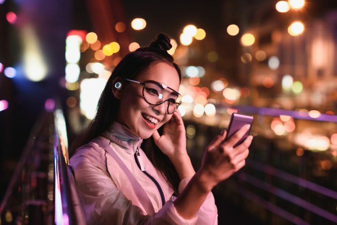 fată fericită asiatică având videochat folosind smartphone și în căști pentru urechi